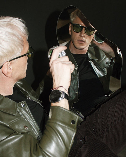 Homme aux cheveux blonds clairs avec un blouson et des lunettes aux verres foncés tenant la boîte de shampoing solide pour homme.