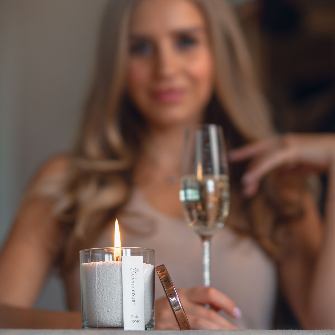 Bougie en poudre Dark Honey allumée, verre de champagne et femme