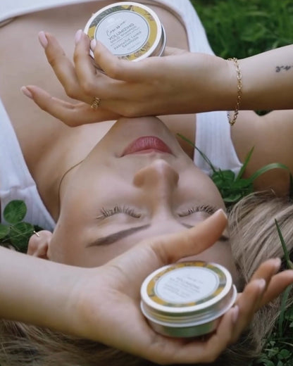 Shampoing et Après Shampoing Solides Tilleul et Bouleau Nordique et leur boîte tenus par une belle femme blonde allongée dans l'herbe